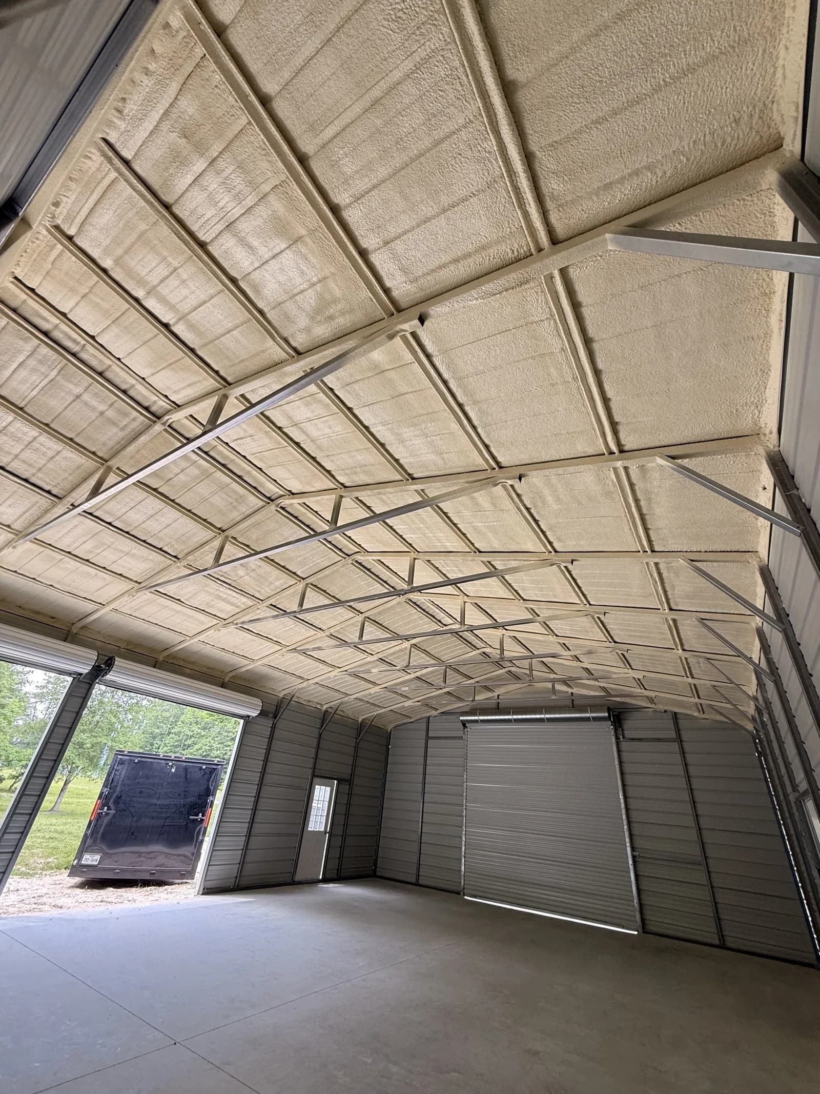Spray foam covering metal roof panels and purlins in a metal shop